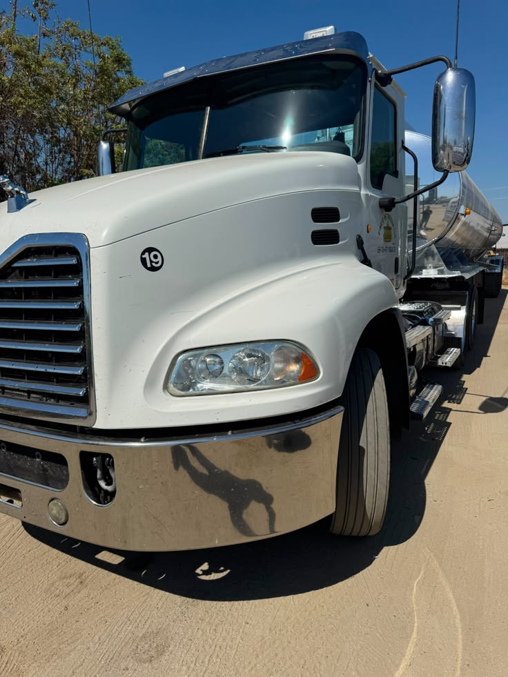 White Mack tanker truck with chrome mirror and silver tank trailer parked outdoors