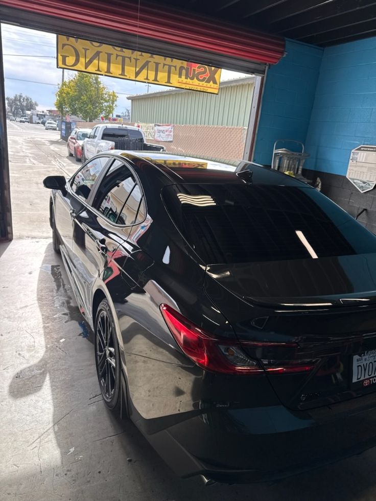 Black sedan parked in auto service bay with blue walls and yellow signage