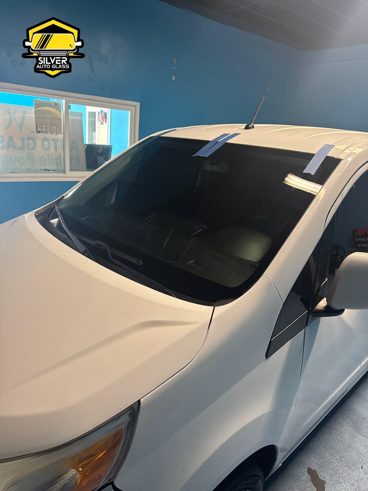 White pickup truck with removed windshield in auto glass shop with blue walls