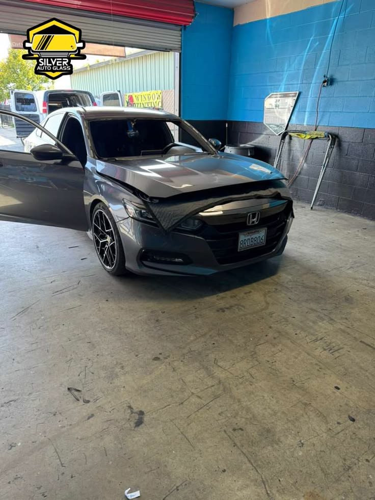 Black Honda with damaged windshield in auto glass shop bay with open hood