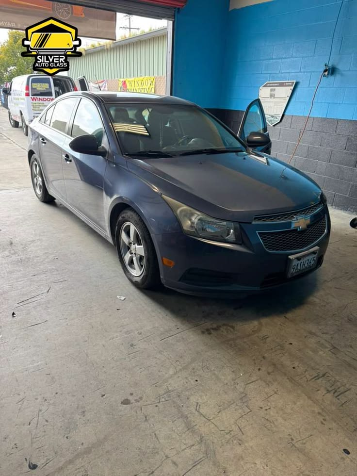 Dark blue Chevrolet Cruze sedan in auto glass shop bay with open driver door