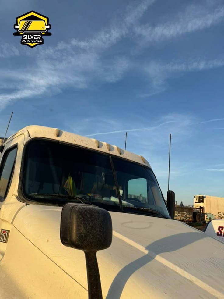 White truck cab with dark mirror against blue sky with Silver Auto Glass logo
