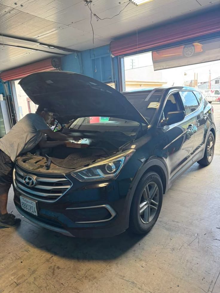Mechanic inspecting engine of dark blue Hyundai Santa Fe in service bay