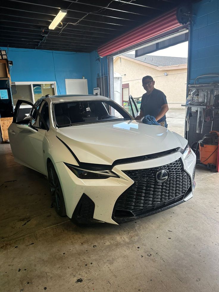Damaged white Lexus sedan in auto body repair shop with technician examining hood