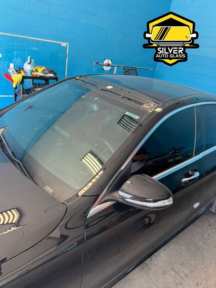 Black car with sunroof being serviced at Silver Auto Glass facility with blue brick wall