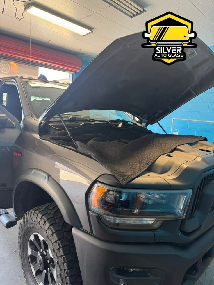 Silver Auto Glass truck with open hood in service bay showing windshield repair work