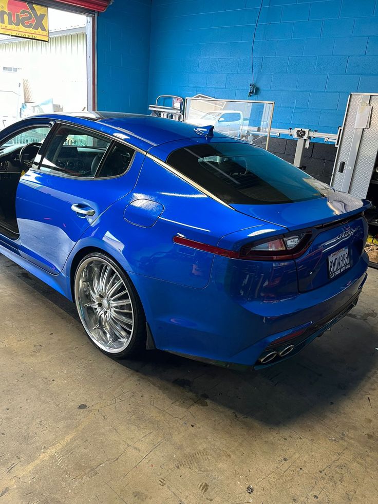 Blue Kia Stinger sedan with custom chrome wheels in auto shop garage