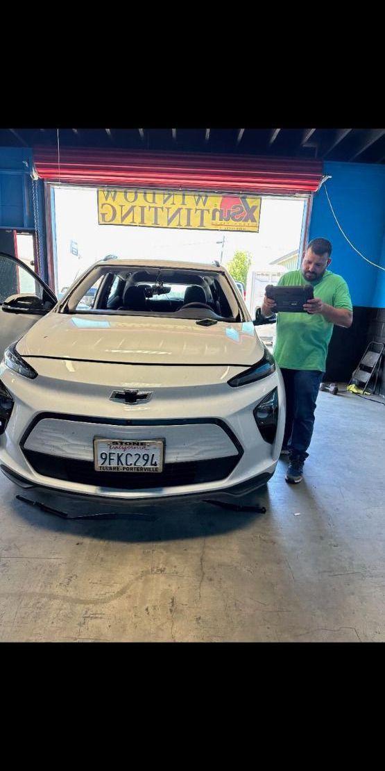 Man in green shirt inspecting white Chevrolet vehicle in automotive service garage